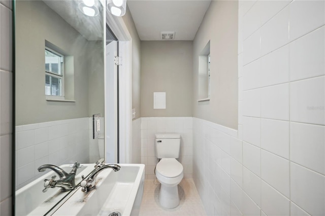 bathroom with tile patterned flooring, toilet, a wainscoted wall, visible vents, and tile walls