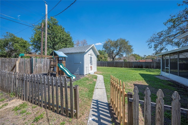 view of yard featuring an outbuilding, a playground, a fenced backyard, and a sunroom