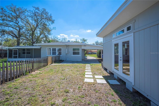 back of property with a lawn, a sunroom, an attached carport, fence, and french doors