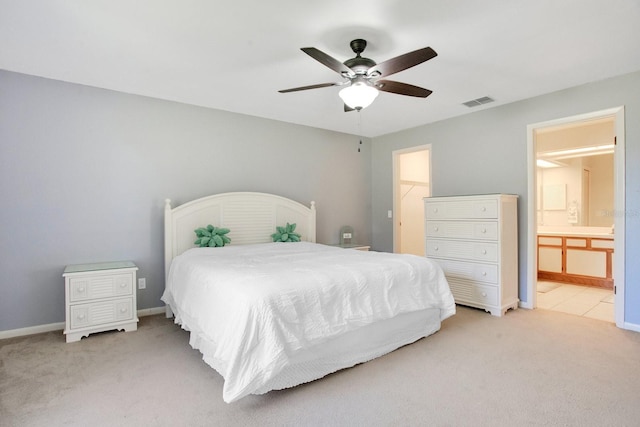 bedroom with connected bathroom, light carpet, visible vents, baseboards, and a walk in closet