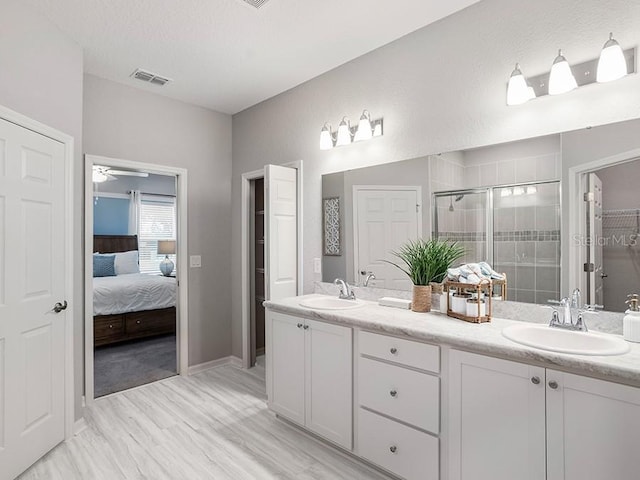 ensuite bathroom featuring double vanity, a sink, visible vents, and a shower stall