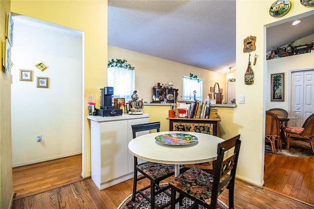 dining area featuring lofted ceiling, a textured ceiling, wood finished floors, and baseboards