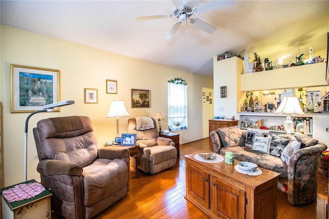 living area with a ceiling fan, vaulted ceiling, a textured ceiling, and hardwood / wood-style flooring