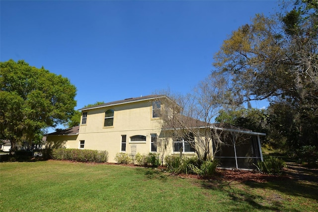 back of property with a sunroom, a lawn, and stucco siding