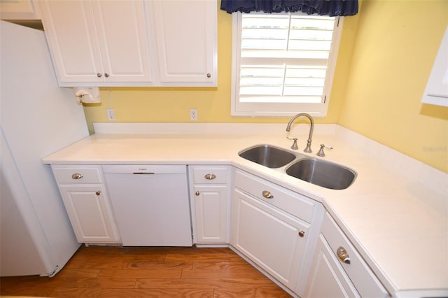 kitchen featuring light countertops, white cabinetry, a sink, wood finished floors, and white appliances