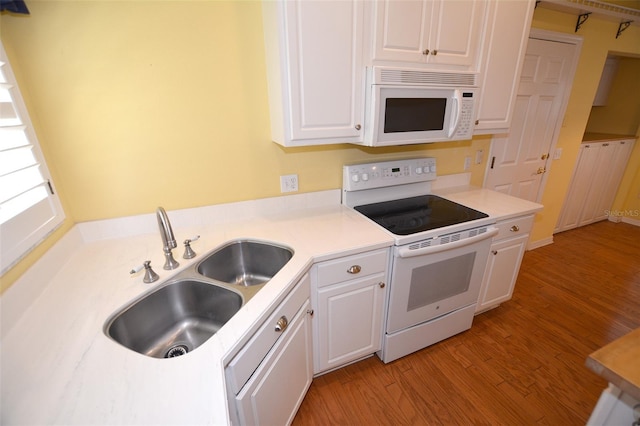 kitchen featuring light countertops, white cabinets, a sink, light wood-type flooring, and white appliances