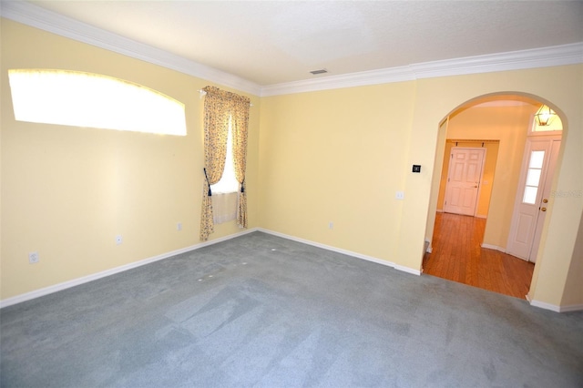 carpeted spare room featuring baseboards, arched walkways, and crown molding