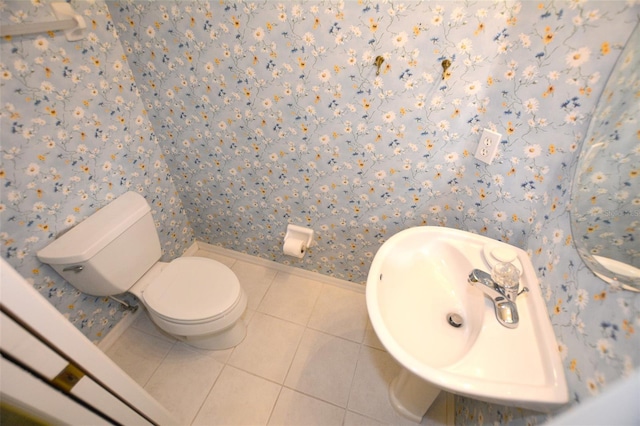 half bath featuring toilet, a sink, tile patterned flooring, baseboards, and wallpapered walls