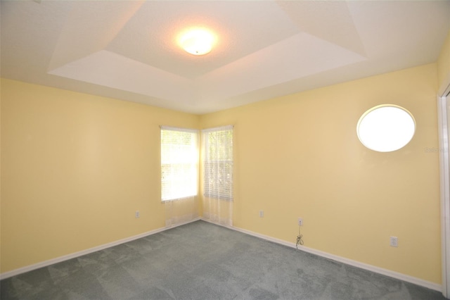 spare room featuring baseboards, a tray ceiling, and dark colored carpet