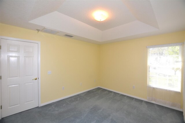 empty room with a tray ceiling, dark carpet, visible vents, and baseboards