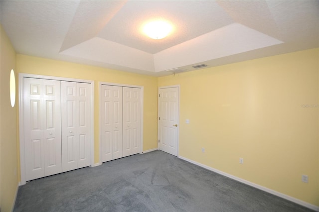 unfurnished bedroom featuring a tray ceiling, multiple closets, visible vents, carpet flooring, and baseboards