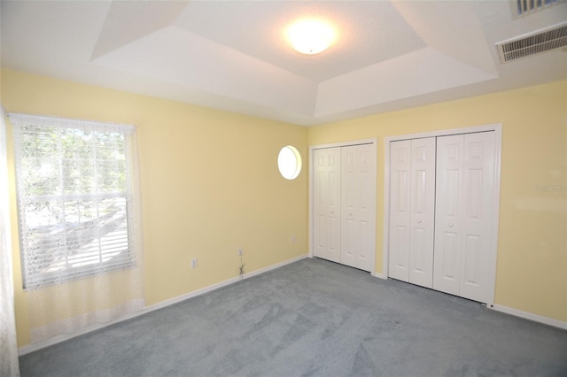 unfurnished bedroom with a tray ceiling, carpet, visible vents, and multiple closets