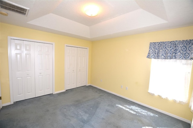 unfurnished bedroom with baseboards, visible vents, a raised ceiling, carpet, and multiple closets