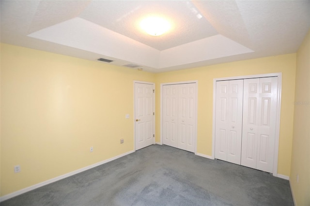 unfurnished bedroom featuring baseboards, dark colored carpet, a tray ceiling, and multiple closets