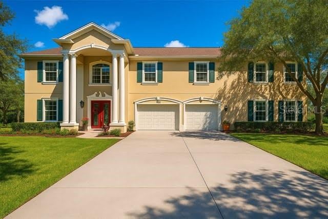 11175 Hyde St, Weeki Wachee, FL 34614 - greek revival house featuring driveway, an attached garage, a front yard, and stucco siding