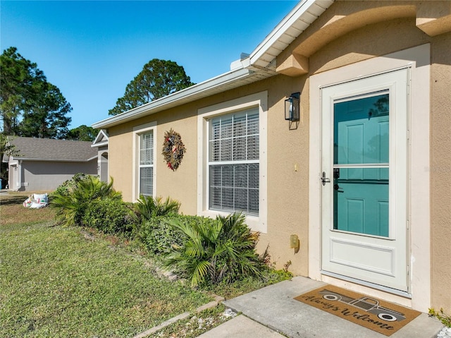 view of exterior entry featuring stucco siding and a lawn