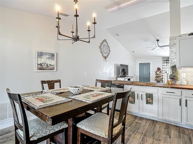 dining space with dark wood-type flooring, ceiling fan with notable chandelier, visible vents, and lofted ceiling