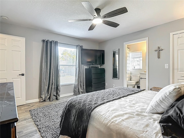 bedroom with baseboards, light wood-style floors, ensuite bath, a textured ceiling, and a ceiling fan