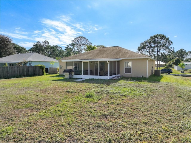 rear view of house with fence, central air condition unit, stucco siding, a yard, and a sunroom