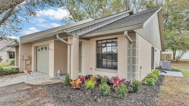 entrance to property featuring a garage, a shingled roof, central AC, and stucco siding