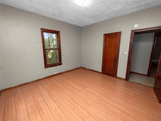 empty room featuring light wood-style floors, baseboards, and a textured ceiling