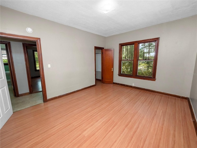 spare room with light wood-type flooring, a textured ceiling, baseboards, and a wealth of natural light