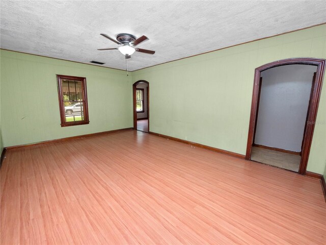 unfurnished room featuring a ceiling fan, visible vents, arched walkways, and wood finished floors