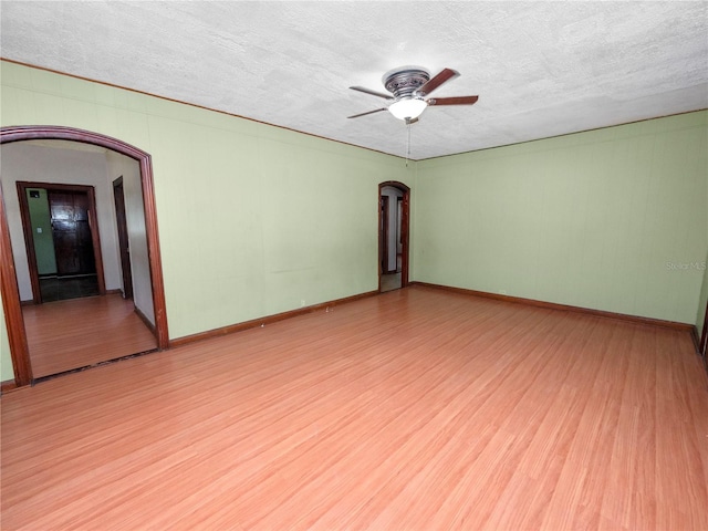 spare room with light wood-style flooring, arched walkways, and a textured ceiling