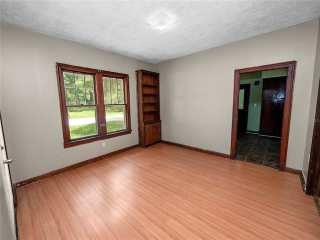 unfurnished room with a textured ceiling, wood finished floors, and baseboards