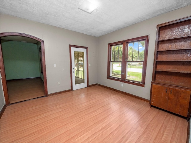 empty room featuring light wood-style floors, baseboards, arched walkways, and a textured ceiling