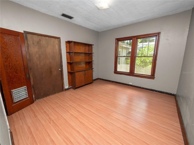 unfurnished room with baseboards, visible vents, light wood-style flooring, and a textured ceiling