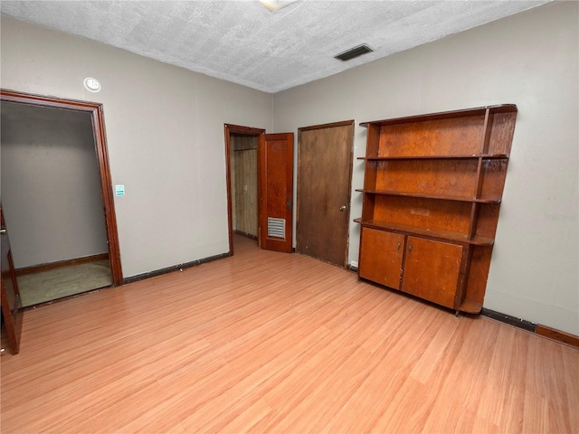 unfurnished bedroom featuring light wood-style floors, visible vents, a textured ceiling, and baseboards