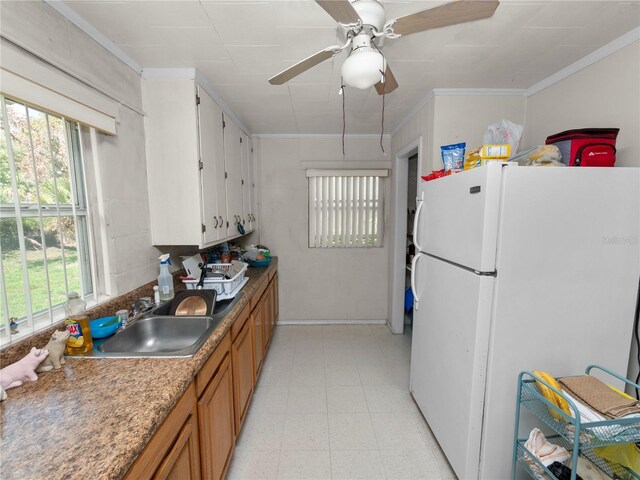 kitchen with brown cabinets, light floors, ornamental molding, freestanding refrigerator, and a sink