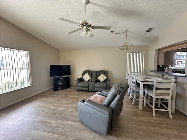 living room with visible vents, vaulted ceiling, a textured ceiling, wood finished floors, and ceiling fan with notable chandelier