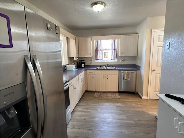 kitchen featuring a sink, wood finished floors, appliances with stainless steel finishes, light brown cabinetry, and dark countertops