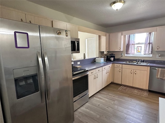 kitchen featuring a textured ceiling, wood finished floors, a sink, appliances with stainless steel finishes, and dark countertops