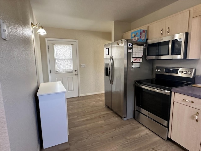 kitchen featuring a textured wall, stainless steel appliances, light brown cabinetry, and light wood-style flooring