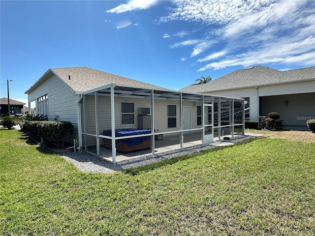 back of property with roof with shingles, a yard, a hot tub, a patio area, and a lanai