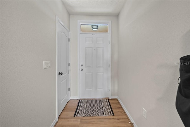 entryway with light wood finished floors, baseboards, and a textured ceiling