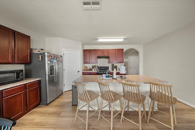 kitchen with visible vents, arched walkways, light wood-style flooring, under cabinet range hood, and black appliances