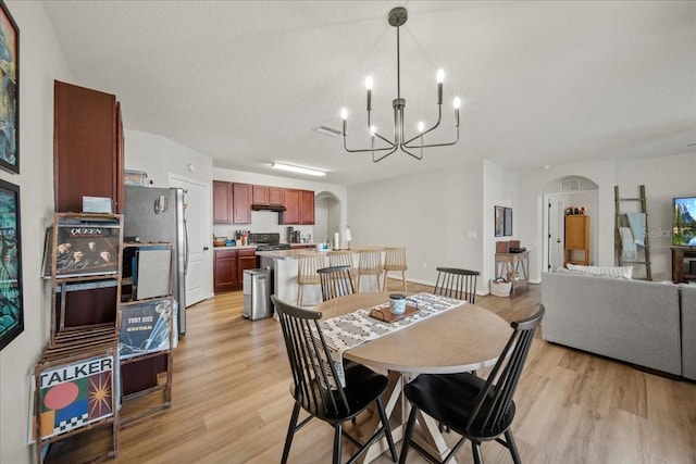 dining space with light wood-style floors, arched walkways, and a notable chandelier