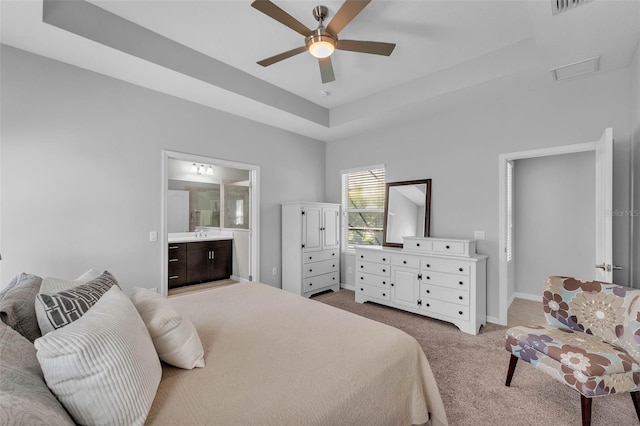 bedroom with a tray ceiling, visible vents, a ceiling fan, light carpet, and connected bathroom