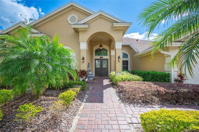 property entrance with a shingled roof, french doors, and stucco siding