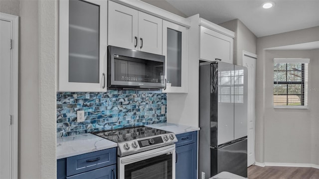 kitchen featuring blue cabinets, white cabinetry, appliances with stainless steel finishes, tasteful backsplash, and glass insert cabinets