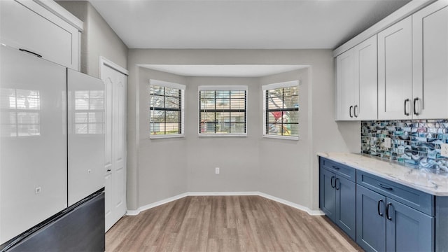 kitchen featuring white cabinetry, baseboards, light wood-style floors, blue cabinetry, and tasteful backsplash