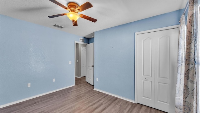 unfurnished bedroom featuring baseboards, visible vents, a ceiling fan, wood finished floors, and a closet