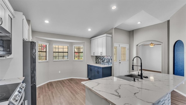 kitchen featuring arched walkways, light wood-style flooring, freestanding refrigerator, a sink, and stainless steel electric range