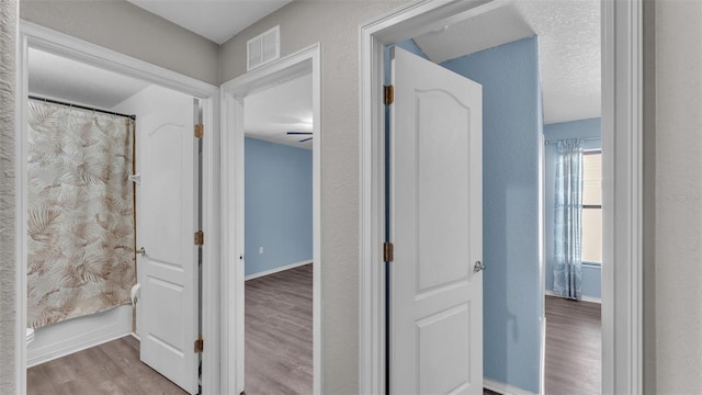 hall with baseboards, visible vents, and wood finished floors