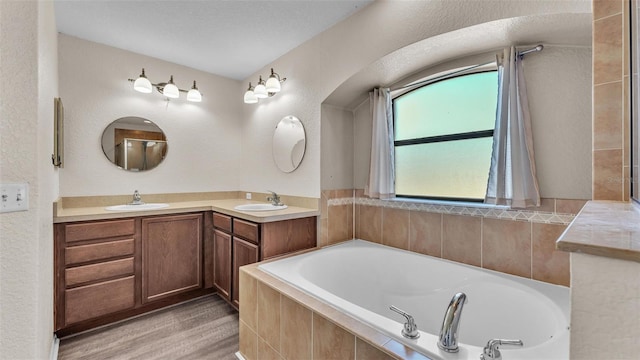 full bath featuring a garden tub, double vanity, wood finished floors, and a sink