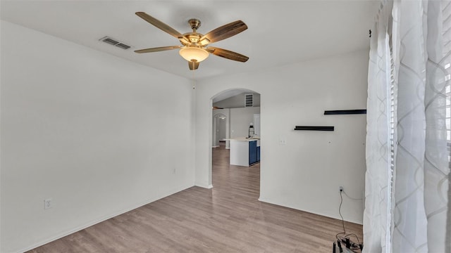 unfurnished room featuring ceiling fan, visible vents, arched walkways, and wood finished floors